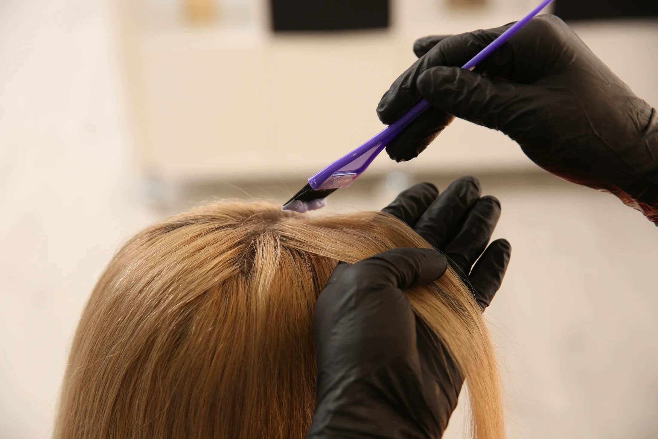Gloved hands applying hair color to roots with a brush