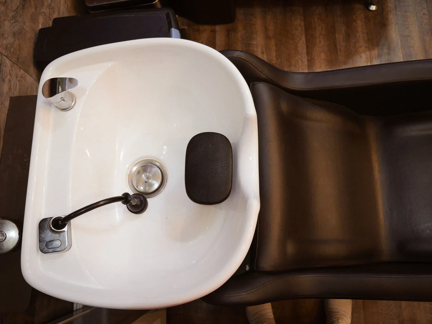 Close-up of a white shampoo basin and dark leather chair